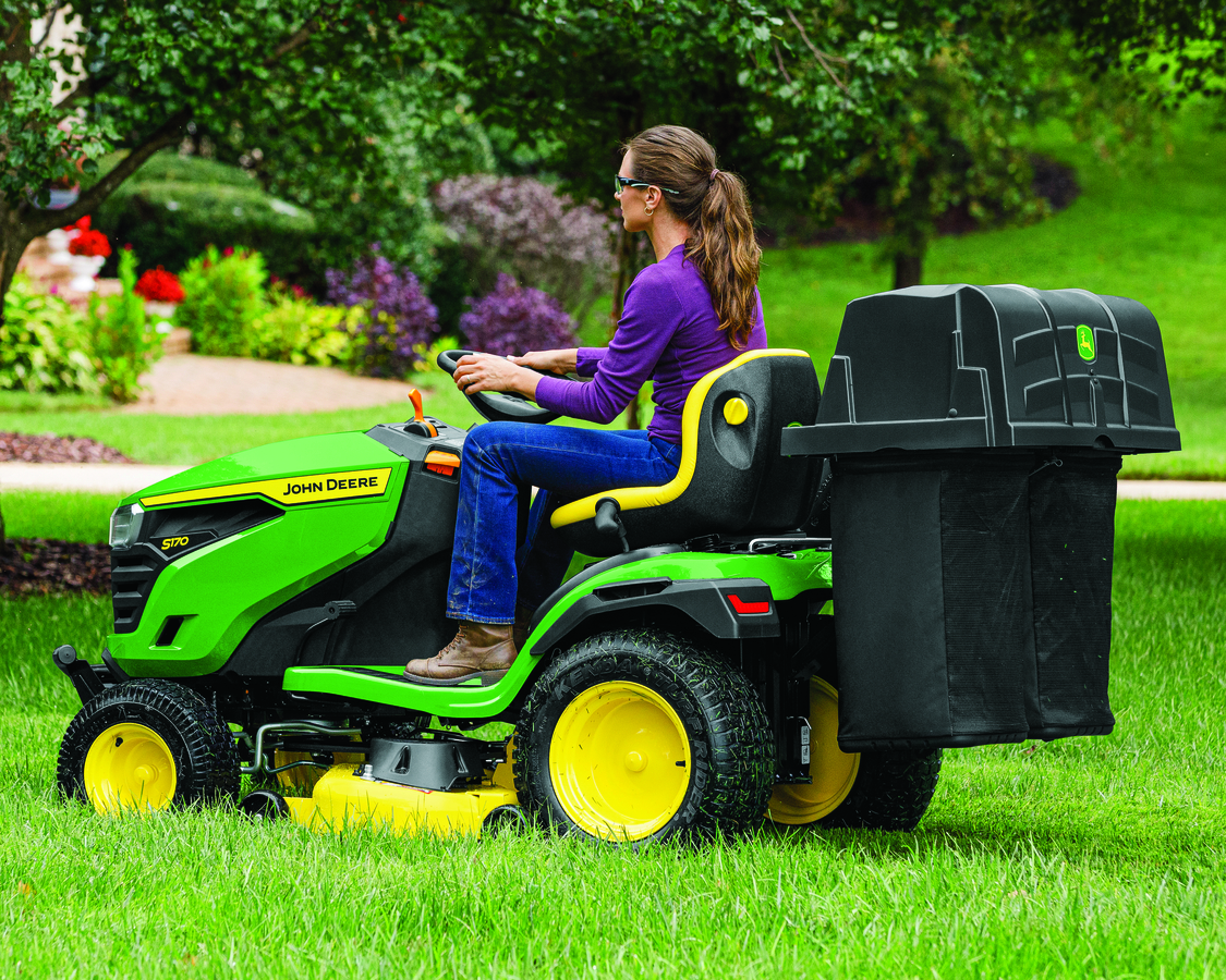 A women is driving a John Deere Lawn Tractor with a Grass Catcher Attachment